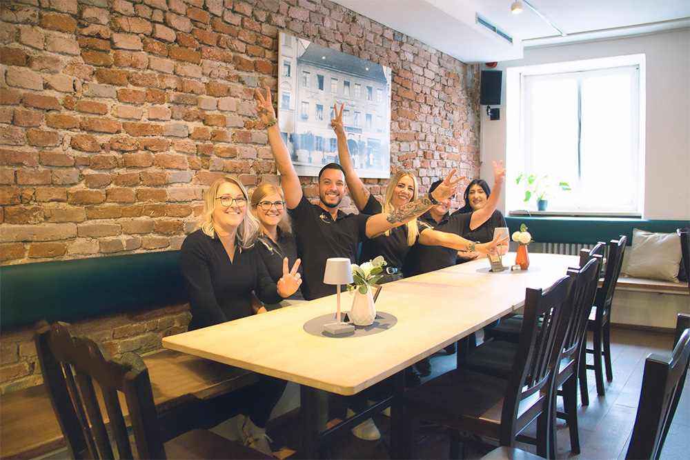 Joelu-Team sitzt an einem Tisch und winkt freudig
